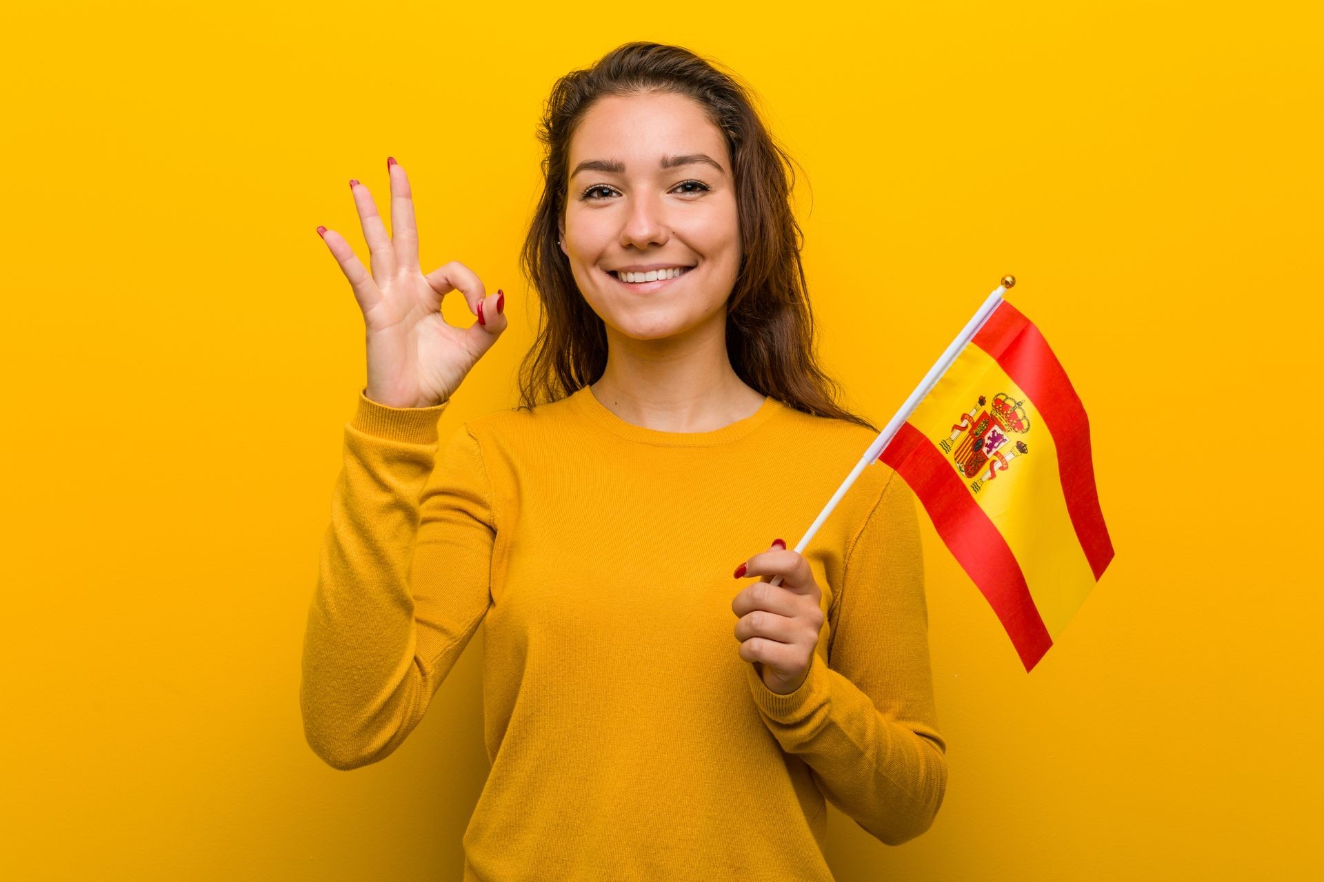 Young european woman holding a spanish flag cheerful and confident showing ok gesture.